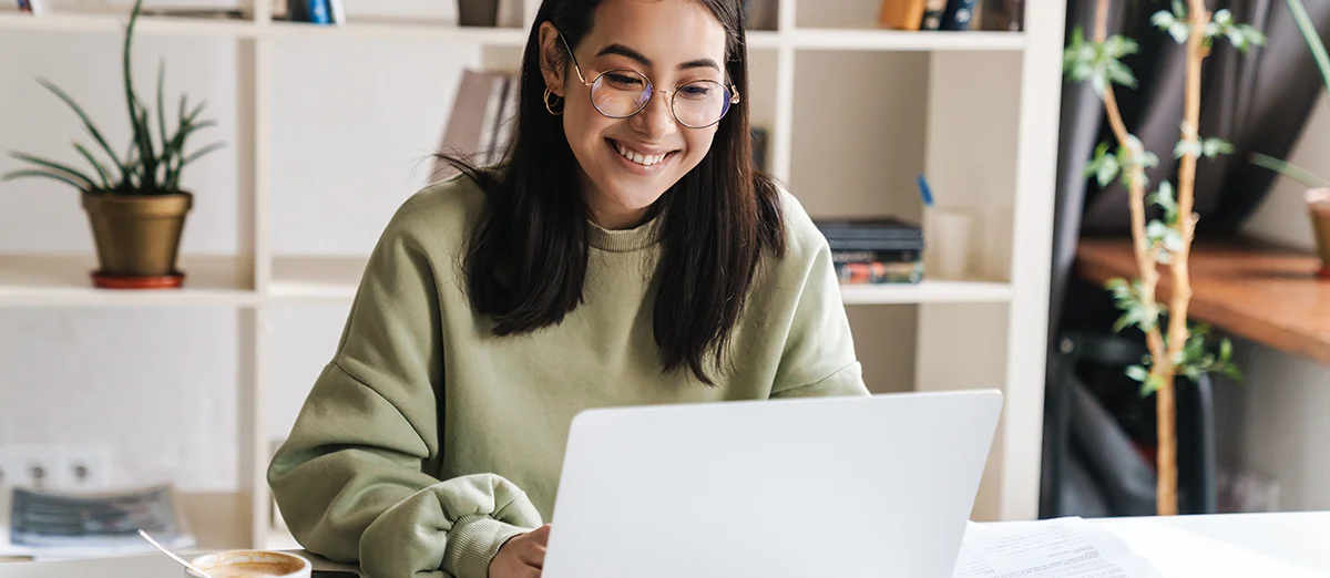 chica sonriente aparece sentada en un escritorio ante un ordenador